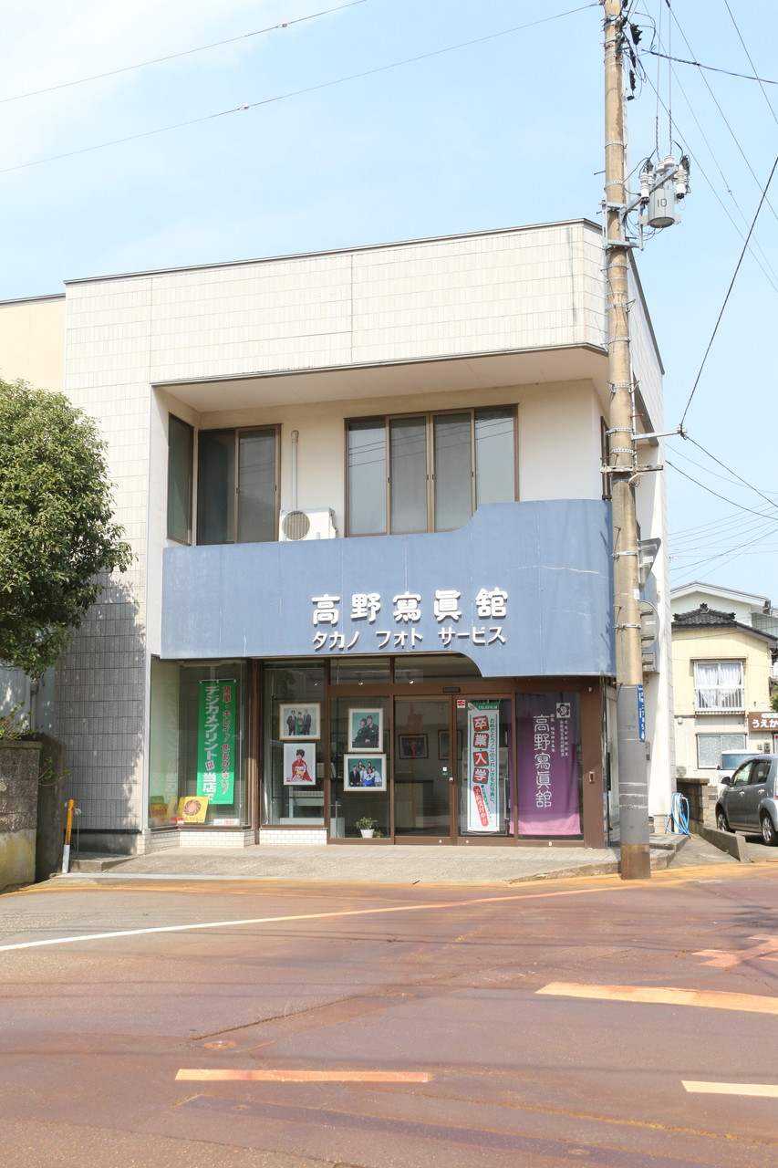 高野寫眞舘の建物全体、2階建ての白い建物に特徴的な青い看板が目立つ外観